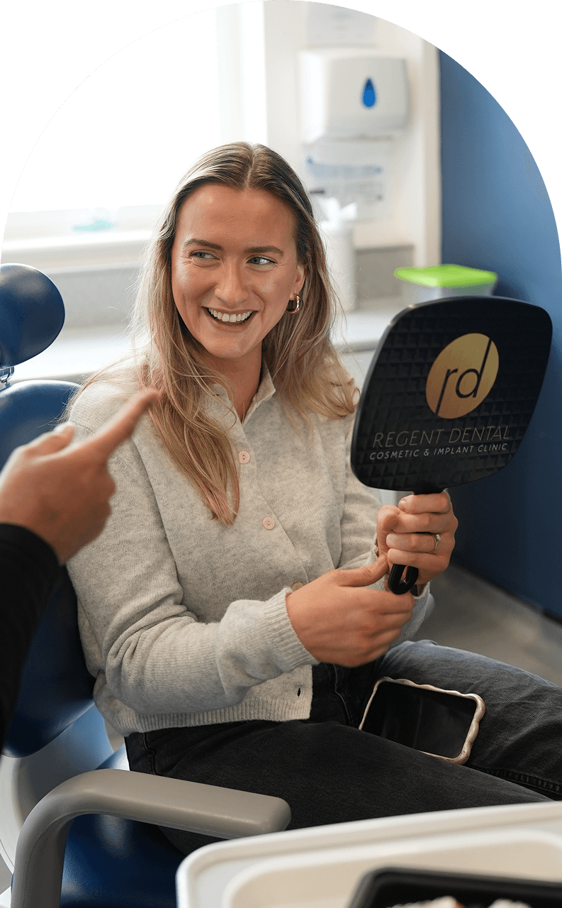 Patient smiling into a mirror during a facial aesthetics consultation at Regent Dental